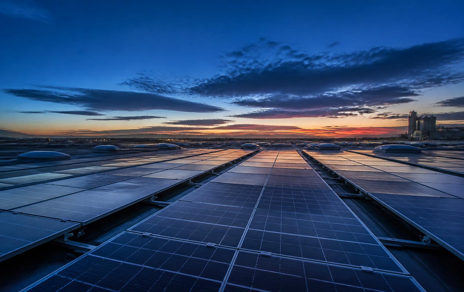 Image d'illustration : rangées de panneaux solaires industriels au crépuscule.